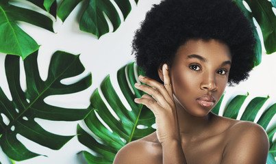 Young and beautiful African woman with perfect smooth skin in tropical leaves