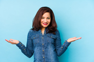 Middle age latin woman isolated on a blue background showing a welcome expression.