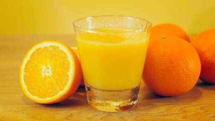 Fototapeta na wymiar Freshly squeezed orange juice in glass, close-up. Glass of orange juice on wooden and yellow background. Orange juice, healthy, organic drink. Glass of orange juice and orange slices.