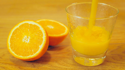Freshly squeezed orange juice in glass, close-up. Pouring orange juice into the glass on wooden background. Orange juice, healthy, organic drink. Glass of orange juice and orange slices.