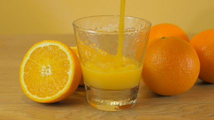 Freshly squeezed orange juice in glass, close-up. Pouring orange juice into the glass on wooden background. Orange juice, healthy, organic drink. Glass of orange juice and orange slices.