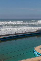 Swimming pool on ocean coast, moviment waves with foam. Wind power. Turquoise water.