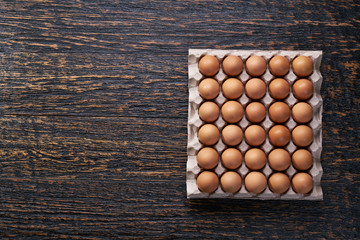 chicken  eggs in a cardboard tray  on a black wooden table, top view.