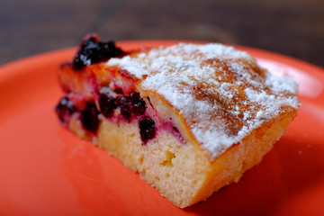 A piece of berry pie dusted with powdered sugar in the plate and a spoon. Close up photo of cake slice. Beautiful and sweet bakery. 