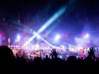 crowd at concert - summer music festival in front of bright stage lights. Dark background, smoke,...