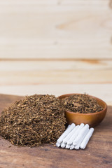 Cigarettes and tobacco in wooden bowl and tobacco joint rolling for smoking.