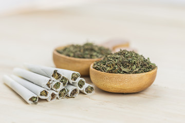 Joint of marijuana. Spoon filled with weed, grinder and wooden background. Rolling a joint and smoking weed.