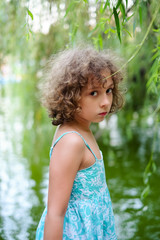 Offended and sad beautiful curly little girl outdoor portrait. Upset child, kid emotions, looking at camera.