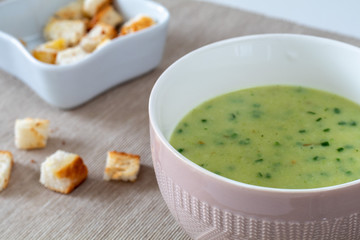 Broccoli cauliflower cream soup with croutons in a brown bowl on a white wooden table and light brown tablecloth.