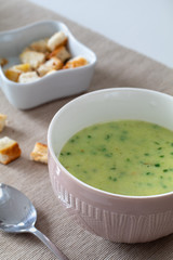 Broccoli cauliflower cream soup with croutons in a brown bowl on a white wooden table and light brown tablecloth