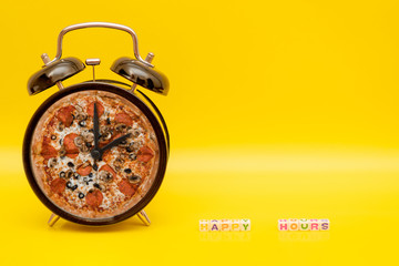 Alarm clock with pizza dial on yellow background with words "Happy Hours" of cube letters
