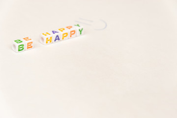 White cubes with colored letters "be happy" on white background with smile is written by pen with copy spase. Mockup