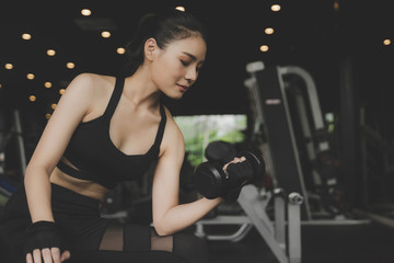 Fototapeta na wymiar athletic young pretty asian slim body woman in black sport bra exercise with dumbbell in fitness gym in background, bodybuilder, healthy lifestyle, exercise fitness, workout and sport training concept