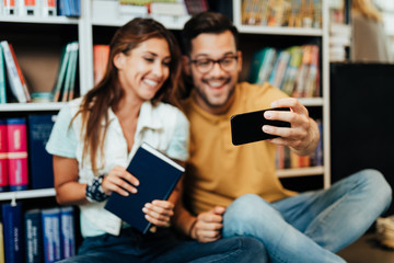 Attractive young students man and woman taking selfie photo in university library.