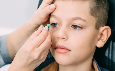 Optometrist trying on a contact lens to a teenage boy. Contact lenses for vision correction in...