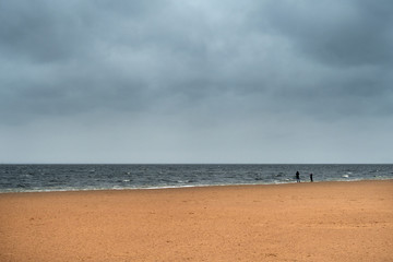 Fototapeta na wymiar Stormy winter beach scene with two silhouette people
