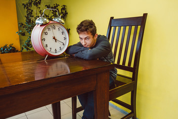 Teenage boy and big alarm clock. Schoolboy is bored on school lesson. Time is long, student guy is waiting for the end of classes in college, university. Endless learning process, study and education.