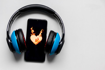 Blauer Funkkopfhörer mit schwarzem Smartphone und brennendem Herz zeigt die feurige Liebe zur...