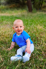 Baby boy sitting on green grass. Beautiful happy little child sitting on a meadow on the nature in the park. Portrait of laughing and smiling cute baby kid.