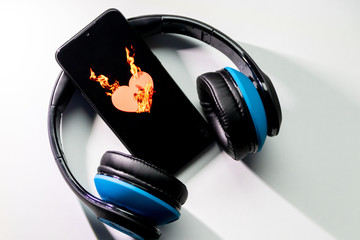 Blauer Funkkopfhörer mit schwarzem Smartphone und brennendem Herz zeigt die feurige Liebe zur...