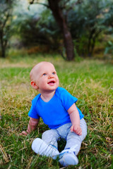 Baby boy sitting on green grass. Beautiful happy little child sitting on a meadow on the nature in the park. Portrait of laughing and smiling cute baby kid.