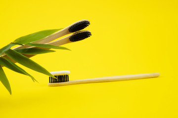Bamboo natural toothbrushes with natural bristles and toothpaste on a yellow background. Wooden...