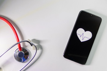 Schwarzes Smartphone mit Herzsymbol und Herzschlag und Stethoskop zeigen digitale Patientenakte, digitale Gesundheitsprogramme und Fitnesstracker in der modernen Gesundheitspraxis