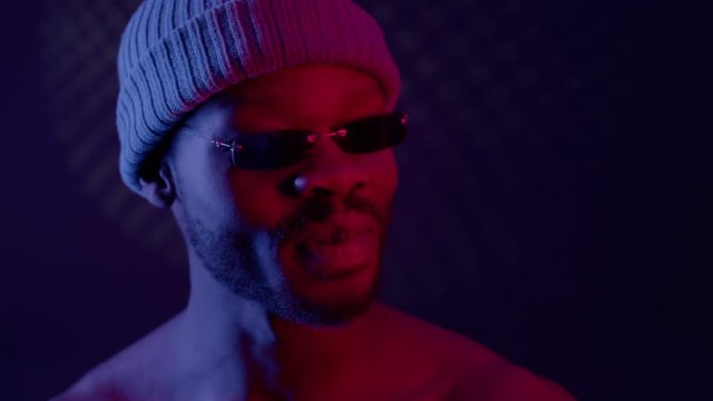 Black Guy In Dark Room With Sunglasses And Cap. Guy Raises His Glasses And Blinks.