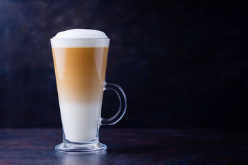 Latte macchiato in a tall glass on a dark background. Cafe latte layered with milk in a high drinking glass. Minimalism. Сopy space