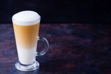 Latte macchiato in a tall glass on a dark background. Cafe latte layered with milk in a high drinking glass. Minimalism. Сopy space