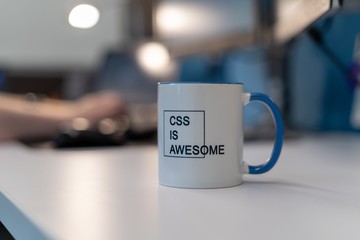 Selective focus shot of a mug with a printed text of "CSS IS AWESOME" with a blurred background
