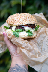 Kobieta niesie dużego hamburgera z mięsem. Kobieca ręka trzyma amerykańską kanapkę na wynos. Street food, slow food. 