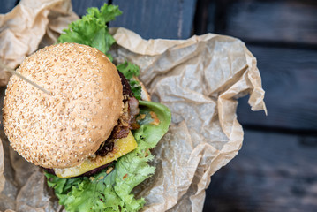 Ujęcie z góry na burgera owiniętego w papier ekologiczny. Kanapka w stylu amerykańskim, bułka sezamowa ze świeżymi warzywami. Slow food.  - obrazy, fototapety, plakaty