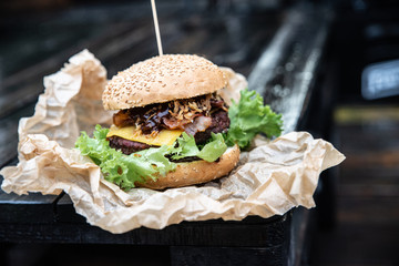 Duży burger w amerykańskim stylu na drewnianym blacie. Kanapka z grillowanym mięsem ze świeżymi warzywami i serem. Hamburger owinęty w papier ekologiczny podany na wynos - obrazy, fototapety, plakaty