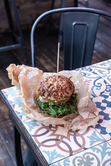 Świeżo grillowany burger leży na stoliku azelejos. Kanapka w amerykańskim stylu zawinięta w papier ekologiczn, street food. Restauracja w industrialnym stylu.  - obrazy, fototapety, plakaty