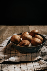 Stock photo of group of Shiitake mushrooms inside blue bowl on tablecloth and natural wooden table with black background.