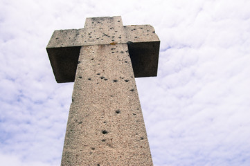 Stone cross with sky background and bullet holes marks from world war 2
