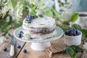 Homemade cherry cake with cream mascarpone on a light background and a bouquet of cherry flowers and lilacs. Horizontal