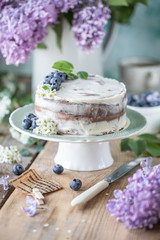 Homemade cherry cake with cream mascarpone on a light background and a bouquet of cherry flowers and lilacs. Vertical