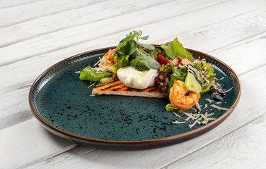 Salad with tiger prawns and poached egg on white wood background.