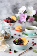 Granola or muesli with berries and fruits for a healthy breakfast in the morning with a bouquet of summer flowers on a light table. Vertical