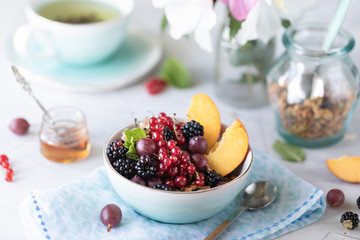 Granola or muesli with berries and fruits for a healthy breakfast in the morning with a bouquet of summer flowers on a light table. Horizontal