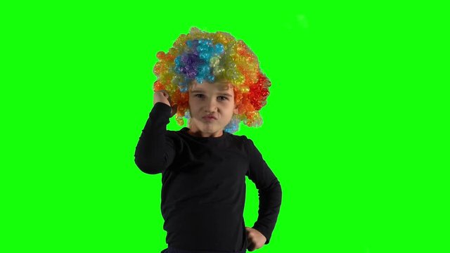 Angry girl with colorful clown wig looking at camera. Child negative emotion