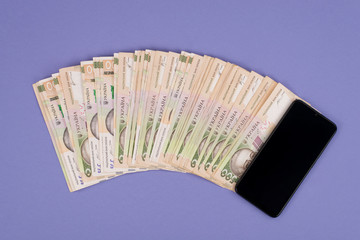 Fan of money concept. Top above close up view photo of smartphone with pile of money isolated purple color background