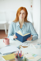 Fototapeta na wymiar Portrait of freckled young woman looking at camera while holding planner at designers workplace