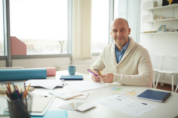 Portrait of mature male designer smiling at camera and holding color swatches while posing at workplace, copy space