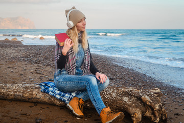 Girl in headphones by the sea reads a book