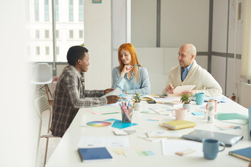 Portrait of mature business people smiling cheerfully while talking to African-American intern during interview meeting in modern white office, copy space