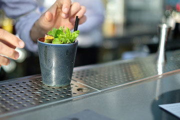 Cocktail being made by male bartender in metal glass on metal bar