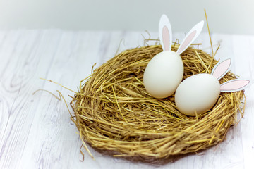 white Easter eggs with rabbit ears in the nest on a wooden table. side view